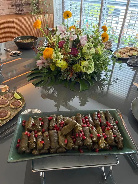 Charutinhos de folha de uva enfileirados em travessa verde, salpicados de romã