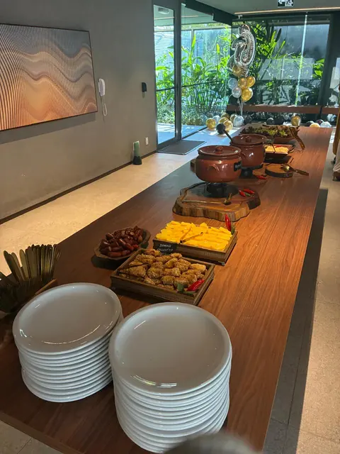 Mesa completa da feijoada com pratos empilhados, acompanhamentos e panelas de barro, num salão com balões