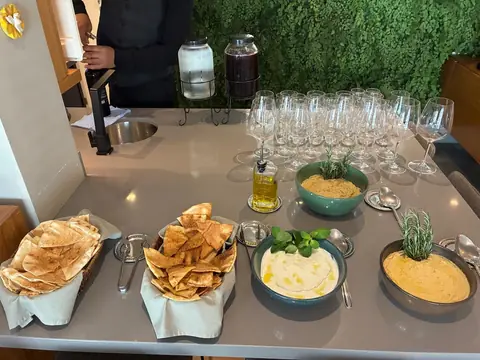 Cesta de chips de pão sírio entre tigelas de homus e coalhada, com taças ao fundo