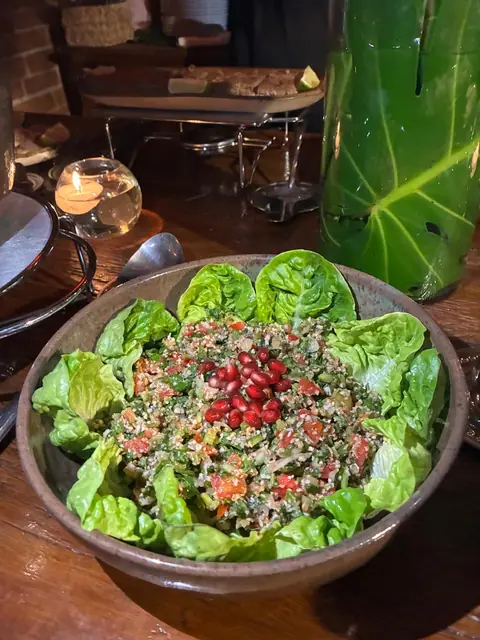 Tabule com tomate e romã servido sobre folhas de alface numa tigela de cerâmica