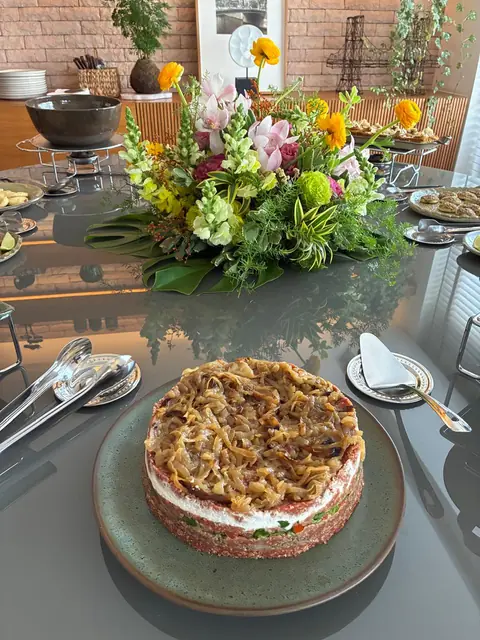 Torre de kibe em camadas coberta com cebola caramelizada, num prato de cerâmica verde